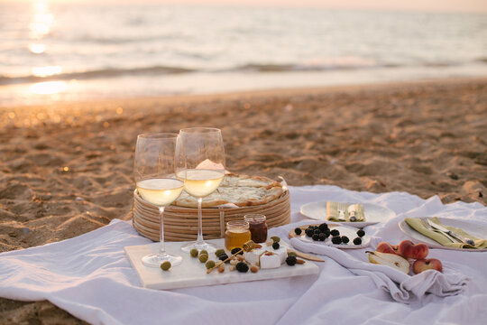 Summer picnic at sunset on beach with white wine, pizza, cheese, olives and fresh fruits.