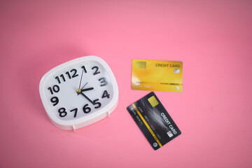 White clock with a credit card on a pink pastel background. Top view