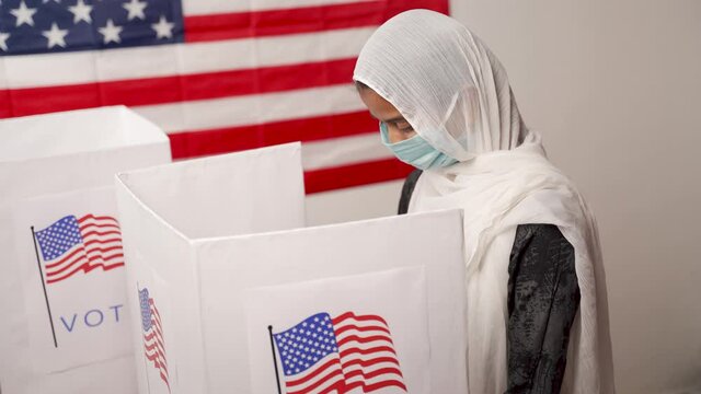Girl with Hijab or head covering and mask worn busy at polling booth with US flag as background - Concept of US election.