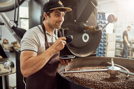 Cheerful man roaster drinking coffee near coffee roasting machine