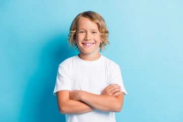 Photo of young kid folded hands curly hairdo toothy smile wear white shirt isolated blue color...