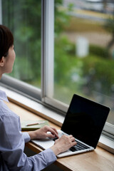 窓際でパソコン操作をする若い女性