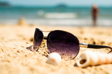 Sunglasses lying on a tropical sandy beach with seashells and stones. Sunglasses on the beach. Nice sea view. Vacation, travel concept