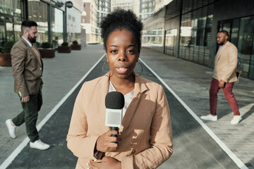 Portrait of African female reporter speaking in microphone she working on the street outdoors