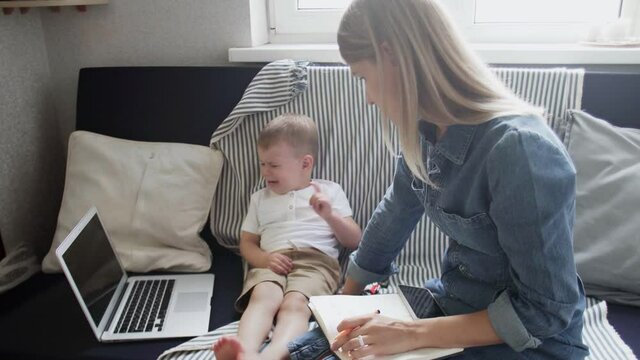 Busy woman tries to work at home, but her naughty son doesn't want watch cartoons on notebook