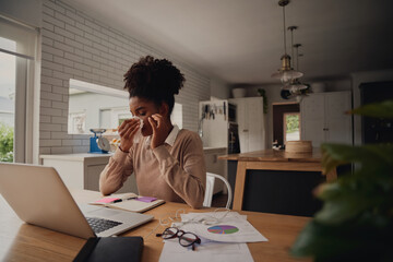 Young female entrepreneur sitting alone blowing nose while using laptop during work from home