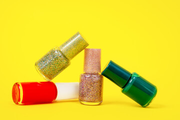 Bottles of multicolored matte and shiny nail polishes with shimmering effect on yellow background, front view, copy space for advertising. Glitter skin decoration for party