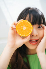 Asian woman wearing green shirt holding slice of oranges.