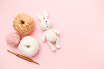White and brown knitting wool, rabbit amigurumi and crochet hook on pink pastel background. Top view, flat lay, copy space