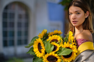 Young happy beautiful girl is walking in dress with a bouquet of sunflowers on a city street. Autumn concept