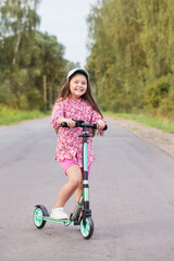 happy little girl riding scooter on country road