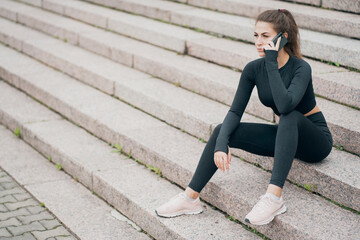 Fototapeta na wymiar portrait of a young woman of athletic build with a brunette smile on her face. sitting on the steps in a beautiful black sports clothes