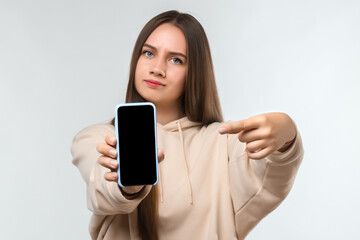 Fototapeta premium Portrait of pretty girl pointing finger at blank screen mobile phone isolated over white background