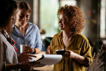 Girlfriends talking and laughing in office. Beautiful women drinking coffee in the office...