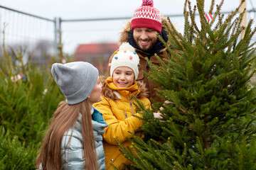 family, winter holidays and people concept - happy mother, father and little daughter choosing christmas tree at street market