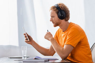 side view of pensive student in wireless headphones using digital tablet at home