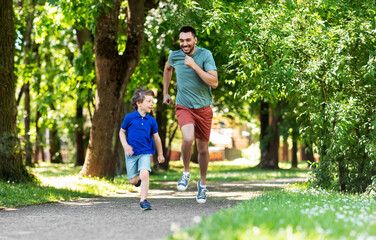 Obraz premium family, fatherhood and people concept - happy father with little son compete in running at summer park