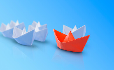 Fototapeta premium red paper boat in front of the white ones. blue background