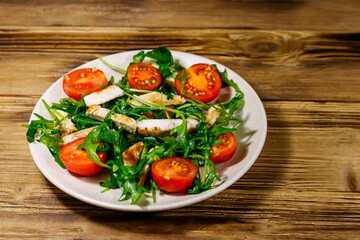 Tasty salad of fried chicken breast, fresh arugula and cherry tomatoes on wooden table