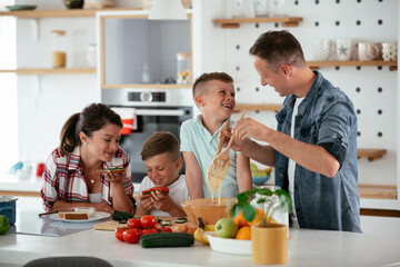  Mother and father making breakfast with sons. Young family preparing delicious food in kitchen