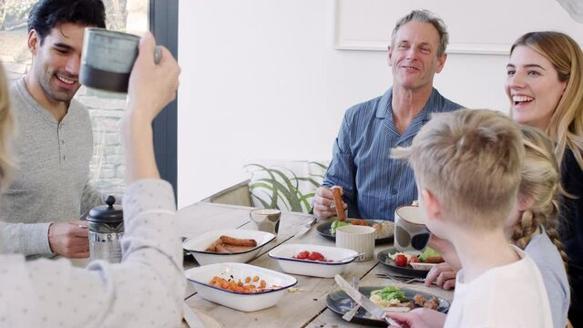 Multi-generation family sitting around table at home in pyjamas enjoying brunch together with grandmother helping granddaughter to cut up food - shot in slow motion