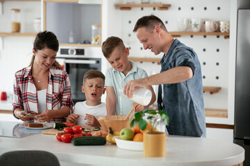  Mother and father making breakfast with sons. Young family preparing delicious food in kitchen