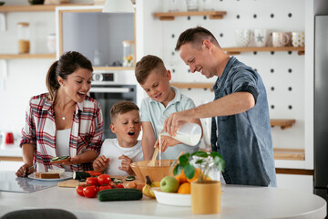 Obraz na płótnie Canvas Mother and father making breakfast with sons. Young family preparing delicious food in kitchen