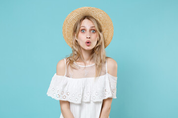 Shocked amazed excited surprised young blonde woman 20s wearing white summer dress hat standing keeping mouth open looking camera isolated on blue turquoise colour background, studio portrait.