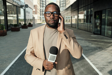 Portrait of African journalist standing with microphone and looking at camera during his work in...