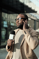 African reporter in eyeglasses speaking in microphone during live broadcasting in the city