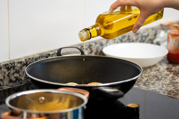 Cropped shot of a woman pouring cooking oil from bottle into frying pan on stove