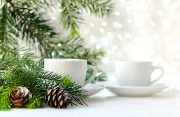Obraz na płótnie Canvas a tree branch, two coffee cups and cones on white background with garlands. The concept of Christmas