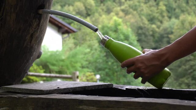 Italy , Alps Devero Piedmont - Mountain wooden fountain - hand filling up a green water bottle cooling  with spring water in nature landscape