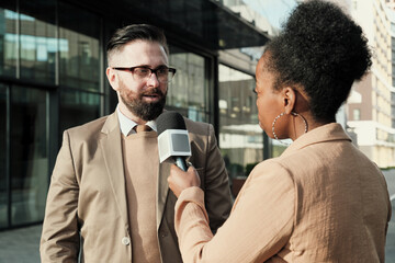 African woman with microphone interviewing the man while they standing in the city