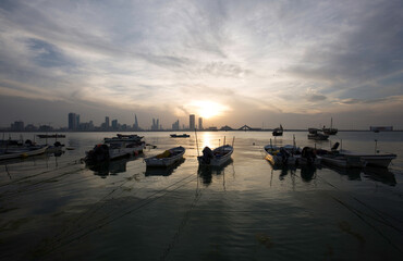 Boats parked at the coast with backdrop of  Bahrain skyline at sunset