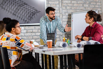 Group of modern business people in casual wear discussing architectural designs while sitting in the creative office.