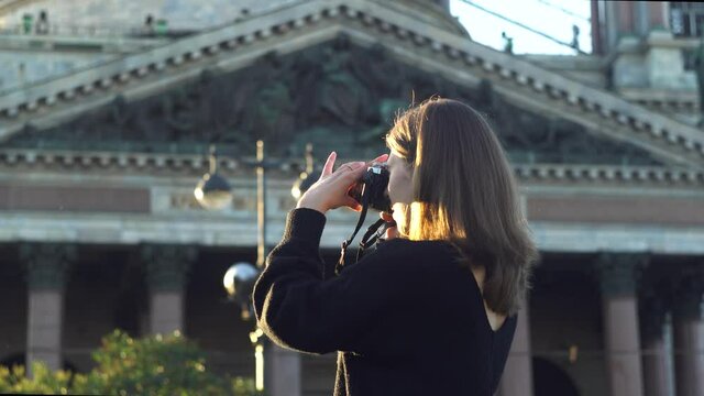 Tourist woman photographing sights. Media. Side view of young female traveler in casual outfit visiting historic building and taking pictures with photo camera during summer holidays.