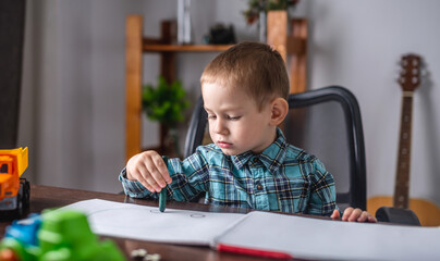 Cute child boy draws with chalk on paper in an album at the table. Preschool education and development of creativity