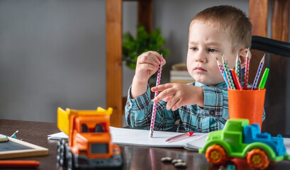 Cute child is drawing with pencils on paper in an album at the table. Preschool education and development of creativity