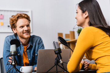 selective focus of brunette asian woman talking to young redhead radio host during interview