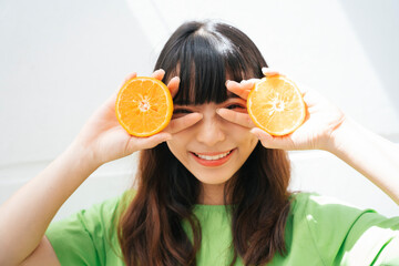 Asian woman wearing green shirt holding slice of oranges.