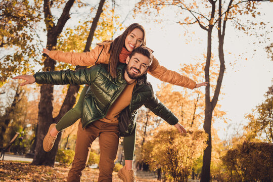 Low angle view photo of romantic couple man carry piggyback girlfriend hold hands in fall city park forest wear coats