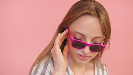 Fototapeta premium Young caucasian woman with sunglasses listening to the music using headphones . Isolated on pink background, close up. High quality photo