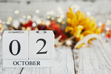 White wood calendar blocks with the date October 2nd and autumn decorations over a wooden table. Selective focus with blurred background.