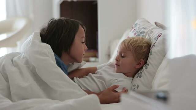 Two sweet children, boy brothers, lying in bed together, talking and smiling
