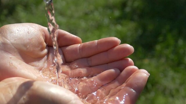Water flows in a stream into the palms of the hands. Pure water from nature