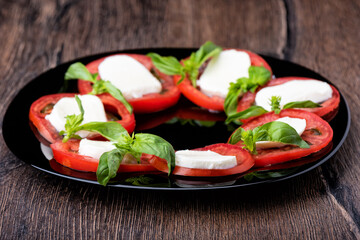 Selective focus. Caprese salad with tomato slices, mozzarella cheese and basil in a black plate on a wooden background.