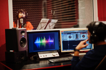 Young asian singer with microphone recording song in record music studio with sound producer.