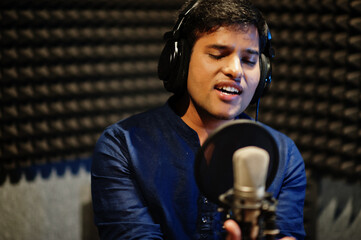 Young asian singer man with microphone recording song in record music studio.