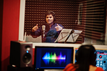 Young asian singer man with microphone recording song in record music studio with sound producer.